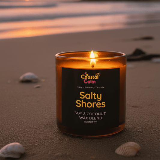 Salty Shore Candle + Coconut Wax Candle by Coastal Calm, glowing in a tranquil beach setting.