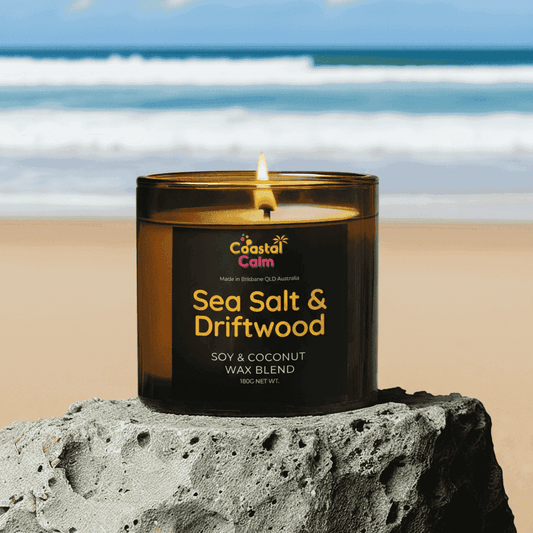 Sea Salt & Driftwood candle by Coastal Calm on a rock with ocean backdrop. Soy & coconut wax blend ideal for coastal home fragrance decor.