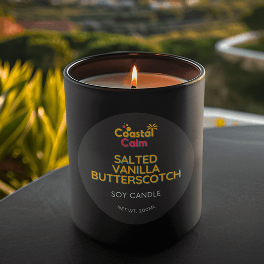Candle labeled 'Coastal Calm Salted Vanilla Butterscotch' with a scenic background