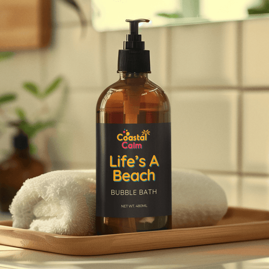 Bottle of 'Coastal Calm Life's A Beach' bubble bath on a wooden tray with towels in a bathroom setting.