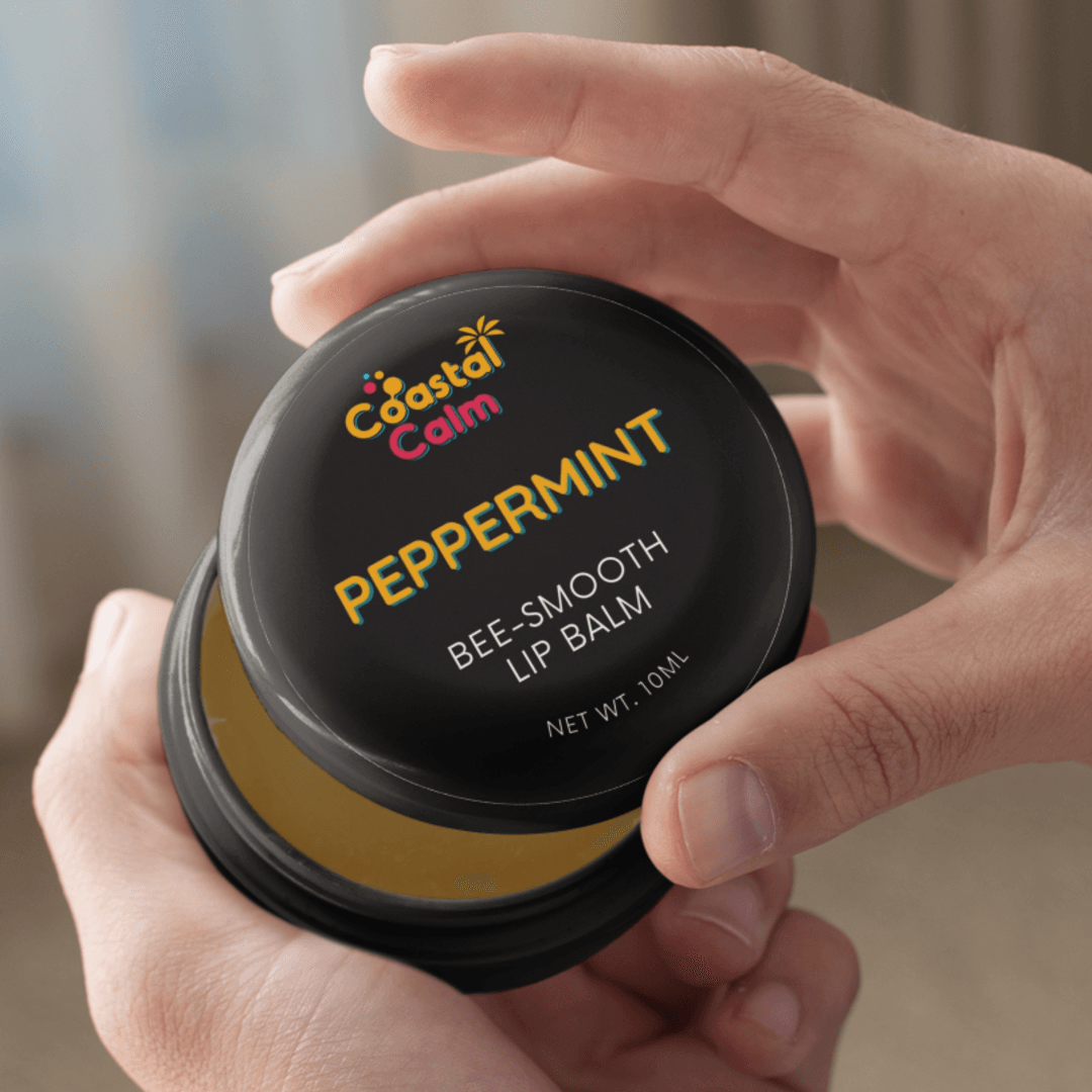 Coastal Calm peppermint lip balm container held by a hand with a blurred background
