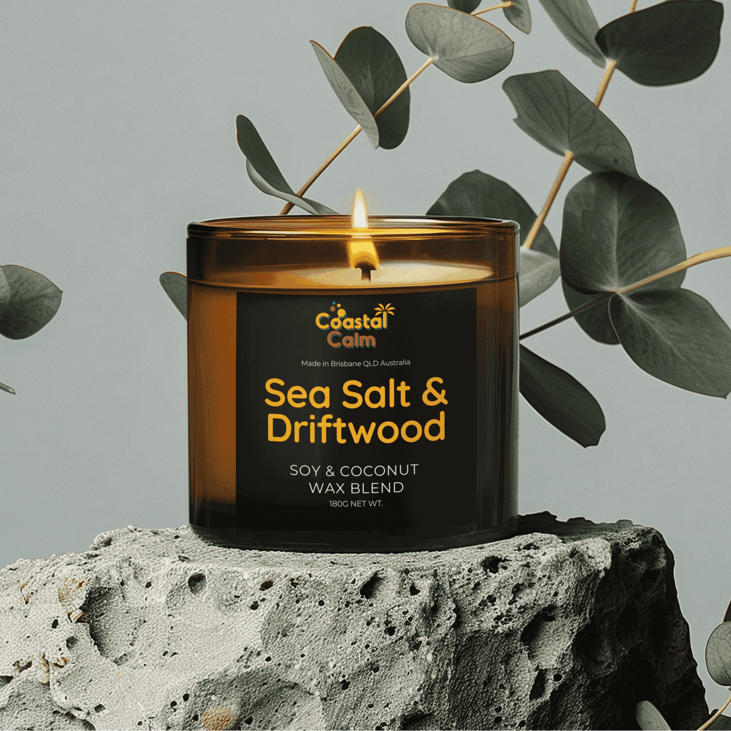 Sea Salt & Driftwood Candle by Coastal Calm with soy & coconut wax blend, placed on stone with eucalyptus leaves, ideal for home fragrance decor.